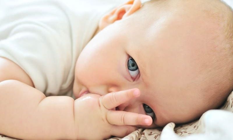 süßes Baby Junge mit grünen Augen saugen seinen Finger