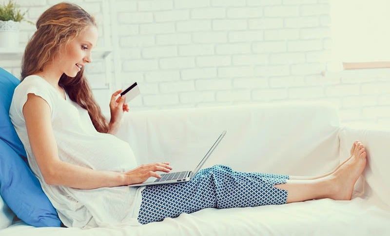 schöne schwangere Frau sitzt auf der Couch mit Laptop und eine Kreditkarte und tun ein Online-Shopping