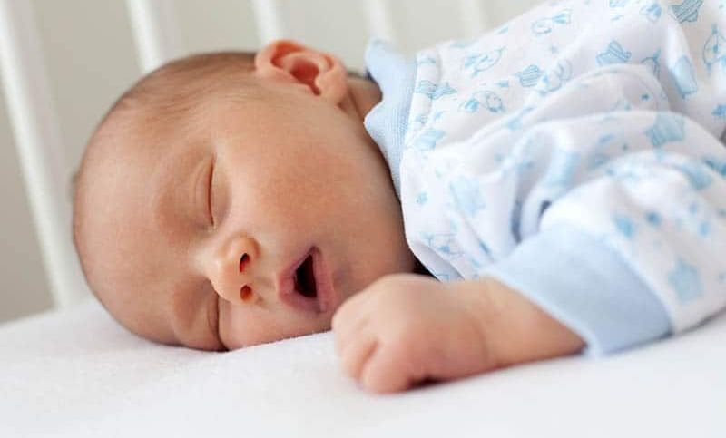 entzückendes neugeborenes Baby, das auf seinem Bauch mit offenem Mund schläft