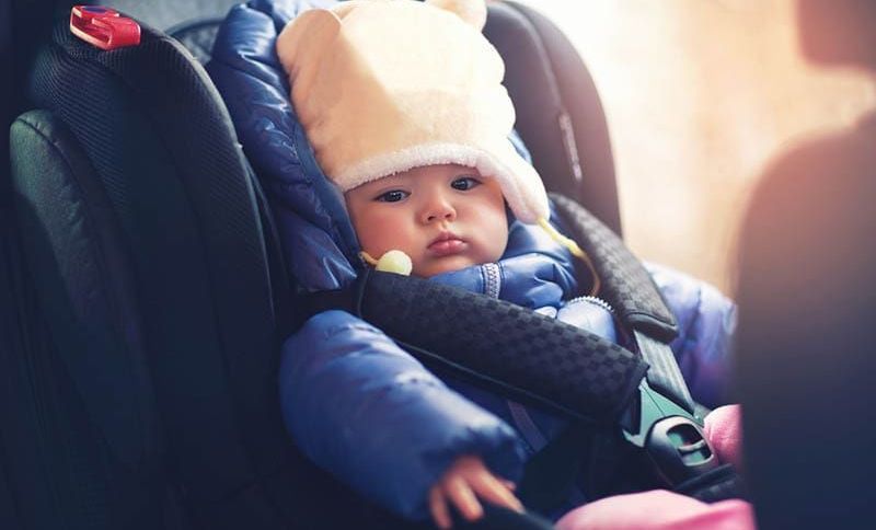 süßes Baby in Winterkleidung in einem Autositz sitzend
