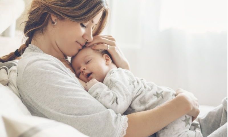 glückliche Mutter, die schlafendes Kleinkind auf Händen hält