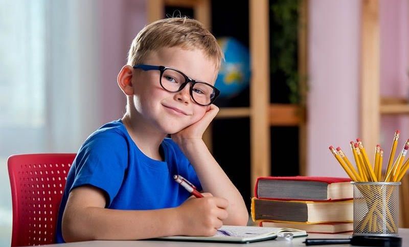 lächelnder kleiner Junge sitzt am Tisch und schreibt in der Schule