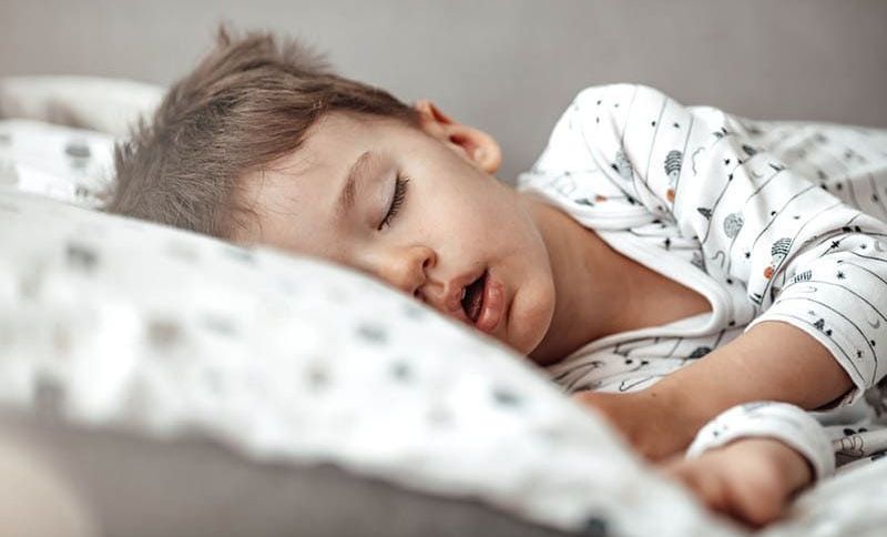 kleiner Junge schlafend im Bett in Pijama mit offenem Mund