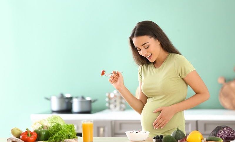 Junge schwangere Frau, die in der Küche isst
