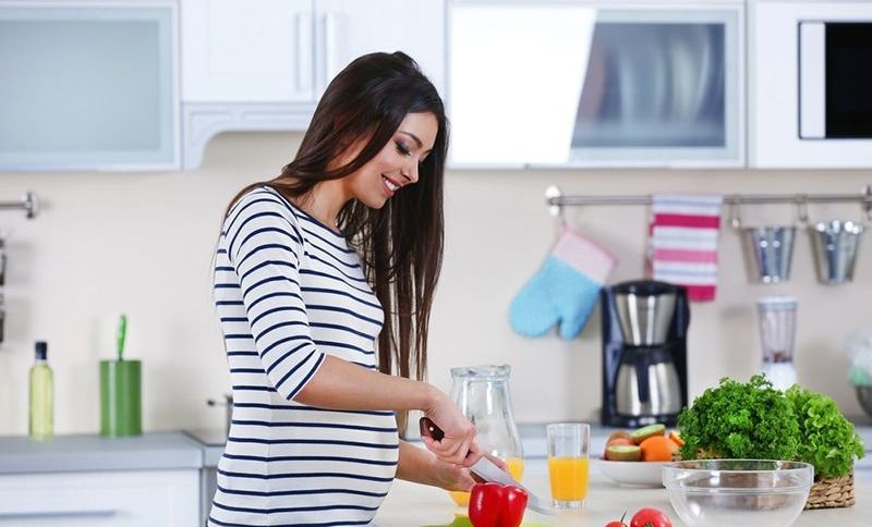 Schwangere Frau bereitet Gemüsesalat am Tisch in der Küche zu