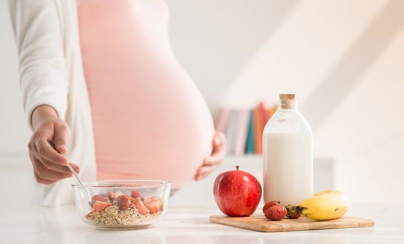 Schwangere Frau, die Mahlzeit mit Milch und Früchten zubereitet