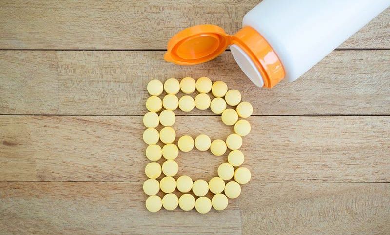 Gelbe Pillen, die auf einem Holztisch die Form des Alphabets B bilden
