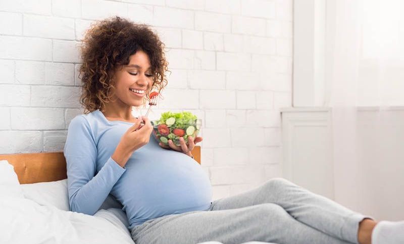 glückliche schwangere Frau essen gesunden Salat auf dem Bett