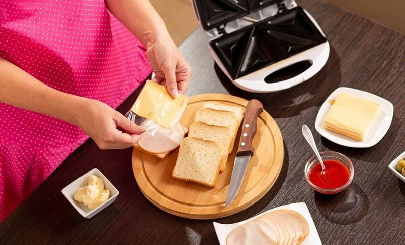 Frau fügt eine Käsescheibe auf ein Sandwich und macht heiße Sandwiches