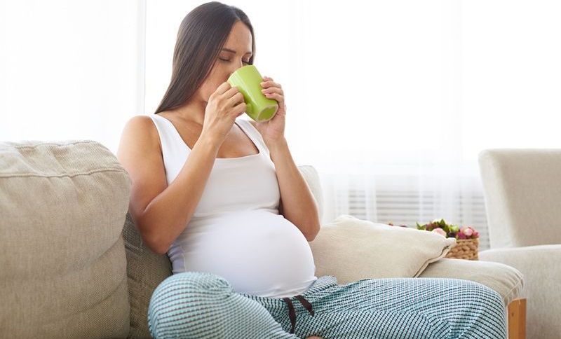 Schwangere trinkt Tee, während sie auf der Couch sitzt