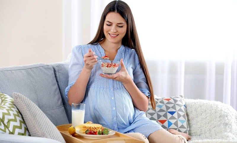 Junge schwangere Frau sitzt auf der Couch und isst
