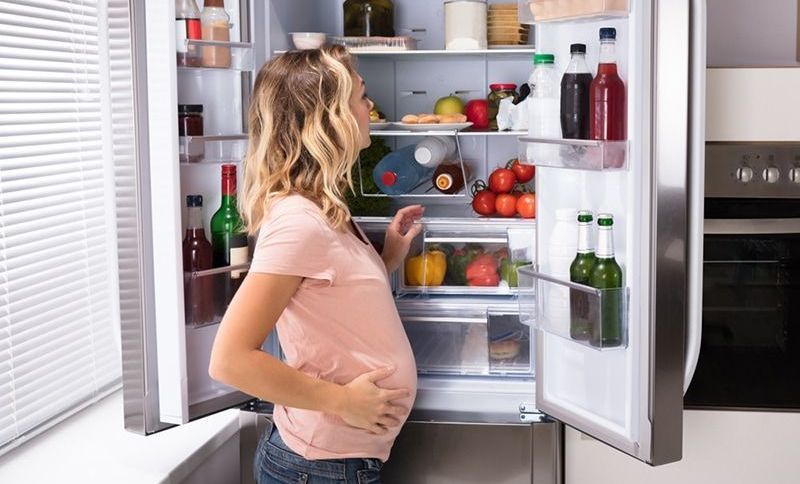 Schwangere Frau auf der Suche nach Essen im Kühlschrank