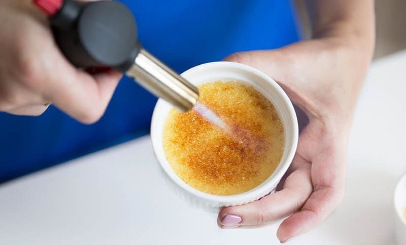 Frau benutzt einen Brenner zum Karamellisieren einer Crème brulee