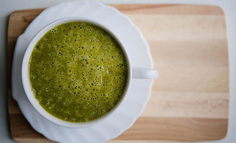 Eine Tasse grüner Smoothie mit Matcha-Tee auf dem Holztisch