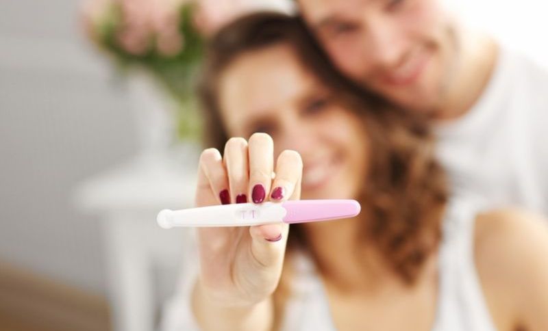 Glückliches Paar mit Schwangerschaftstest im Schlafzimmer