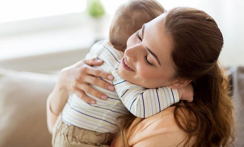 lächelnd Mutter umarmt mit ihrem Baby Sohn auf der Couch zu Hause