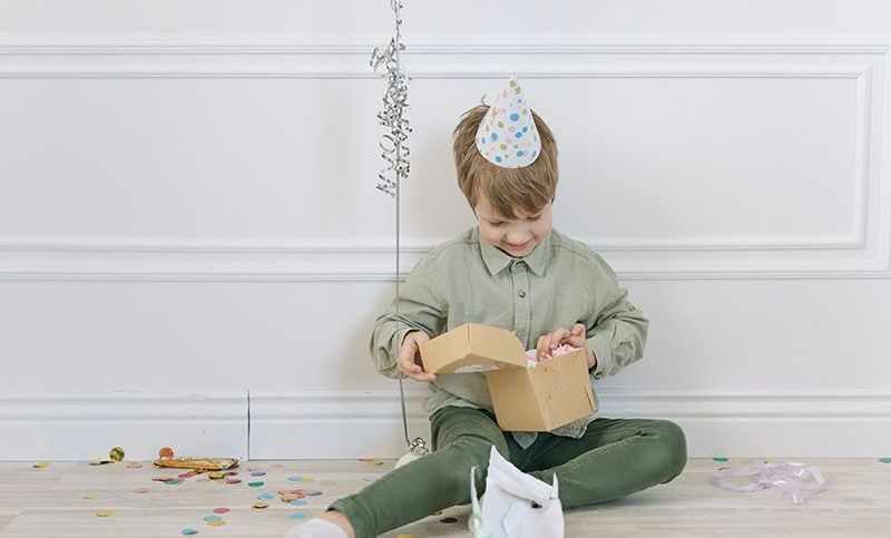 ein kleiner Junge, der auf einer Geburtstagsfeier eine Geschenkbox öffnet