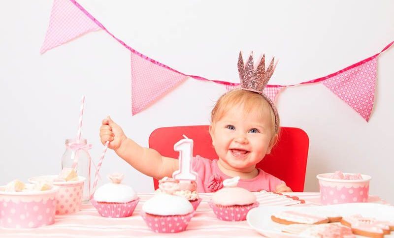 niedlichen Baby Mädchen feiert ihren ersten Geburtstag mit Süßigkeiten auf dem Tisch