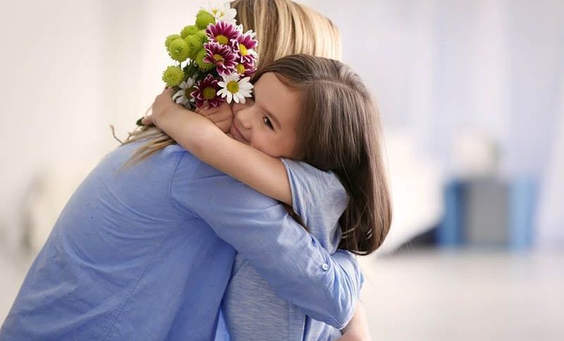 niedlichen kleinen Mädchen umarmt Mutter und geben ihr Blumen