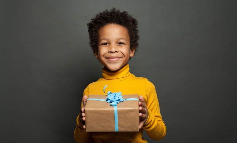 süßer kleiner Junge im gelben Rollkragenpullover lächelt und hält ein Geschenk