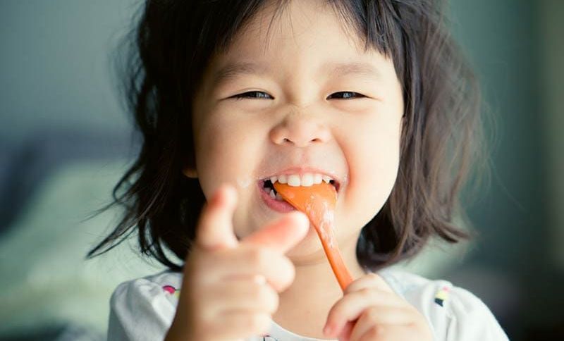 glücklich asiatische Mädchen miling mit Löffel im Mund