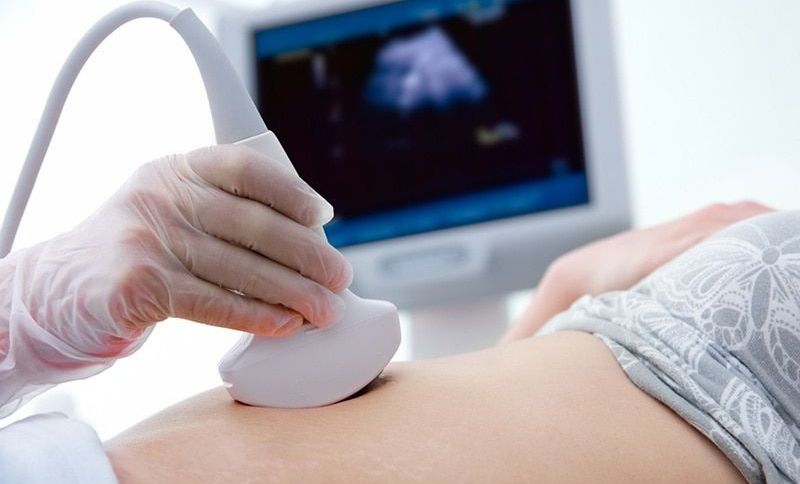 schwangere Frau, die eine Ultraschalluntersuchung des Babys vom Arzt mit Handschuh erhält