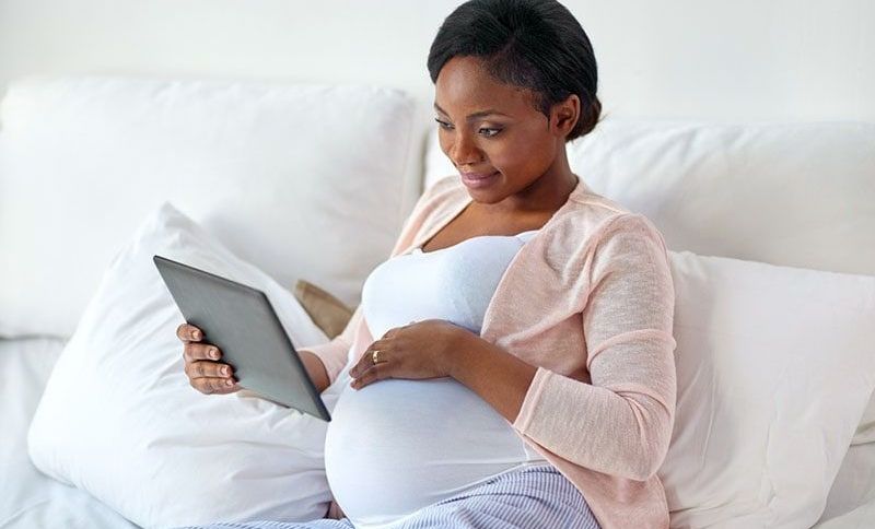 junge schwangere Frau, die Artikel auf Tablette liest