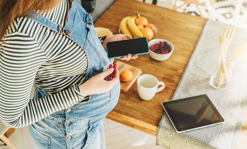 schwangere Frau, die Telefon hält und Obst isst