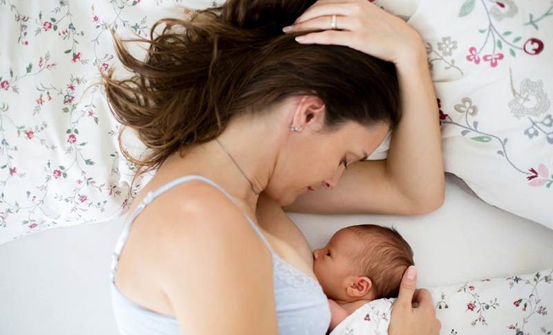 junge Mutter stillt ihr neugeborenes Baby im Bett auf floralen Laken